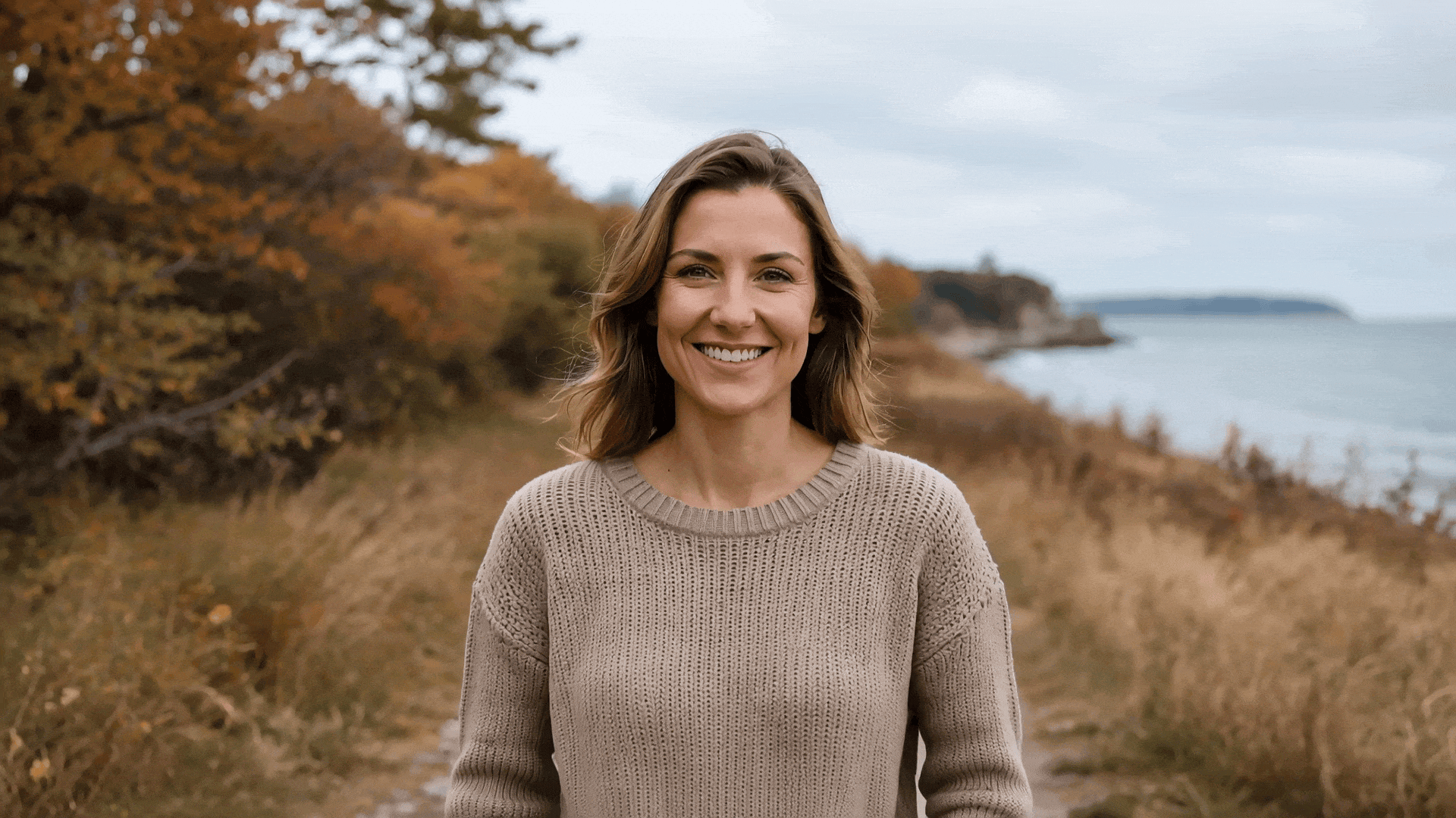 HappyHorse 1.0 (Image-to-Video Focus):
Prompt: "The woman looks directly at the camera and smiles warmly, natural wind blowing her hair, soft overcast daylight, shallow depth of field, 35mm lens."