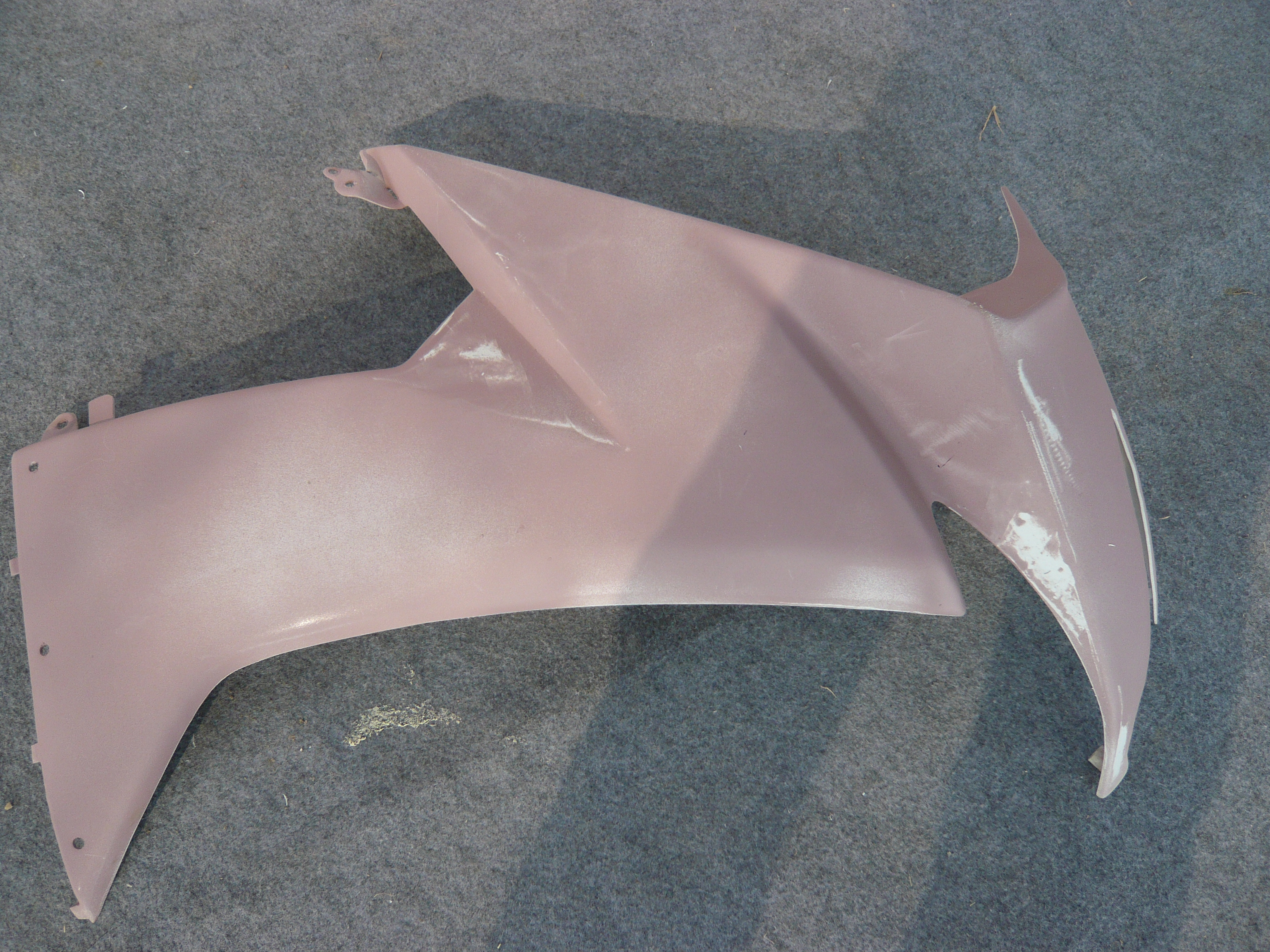 Unpainted side fairing panel during surface preparation in the NiceFairings workshop, photographed alone on a grey floor.