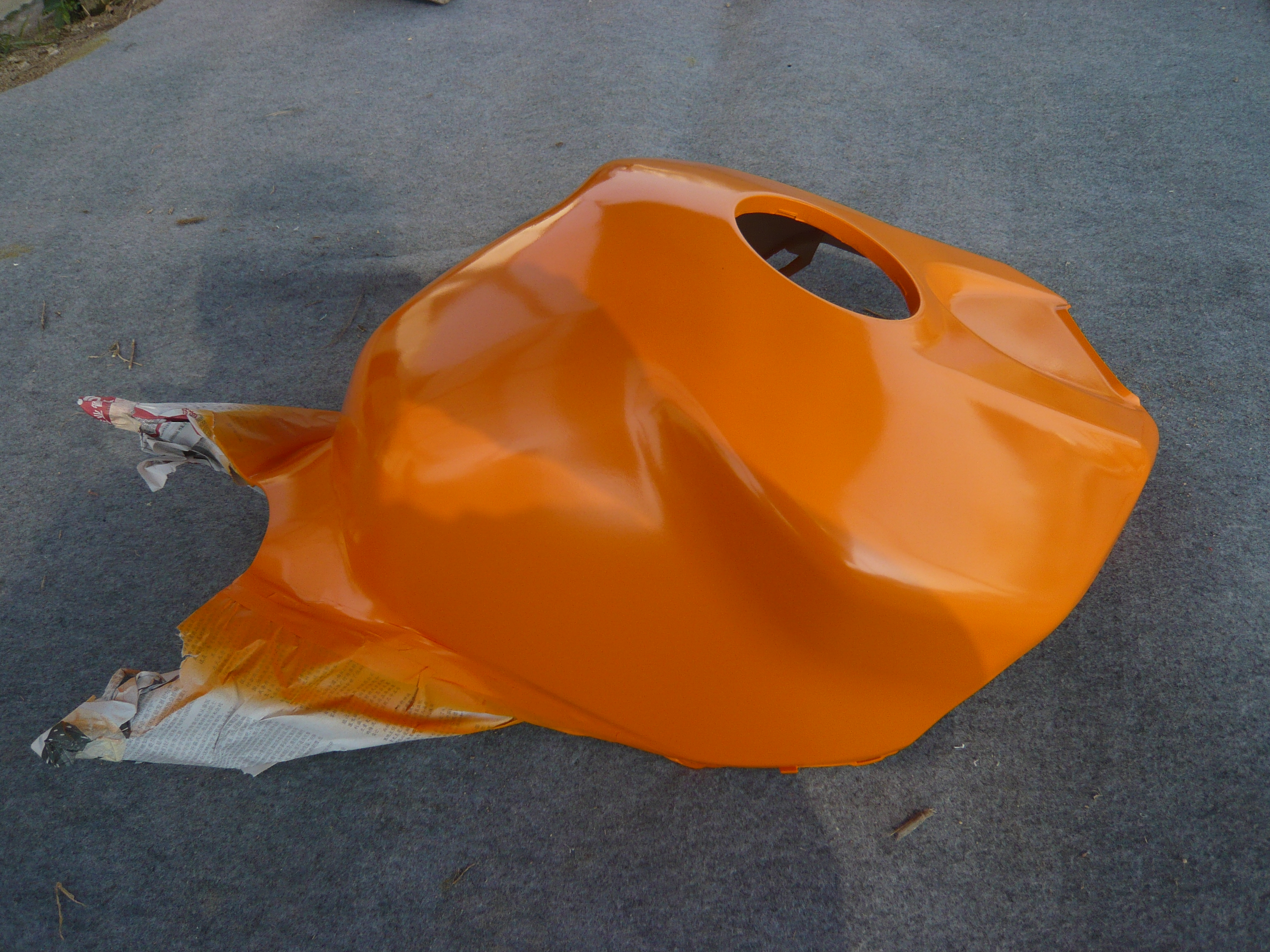 Orange tank-cover-shaped fairing component photographed during paint work in the NiceFairings workshop.