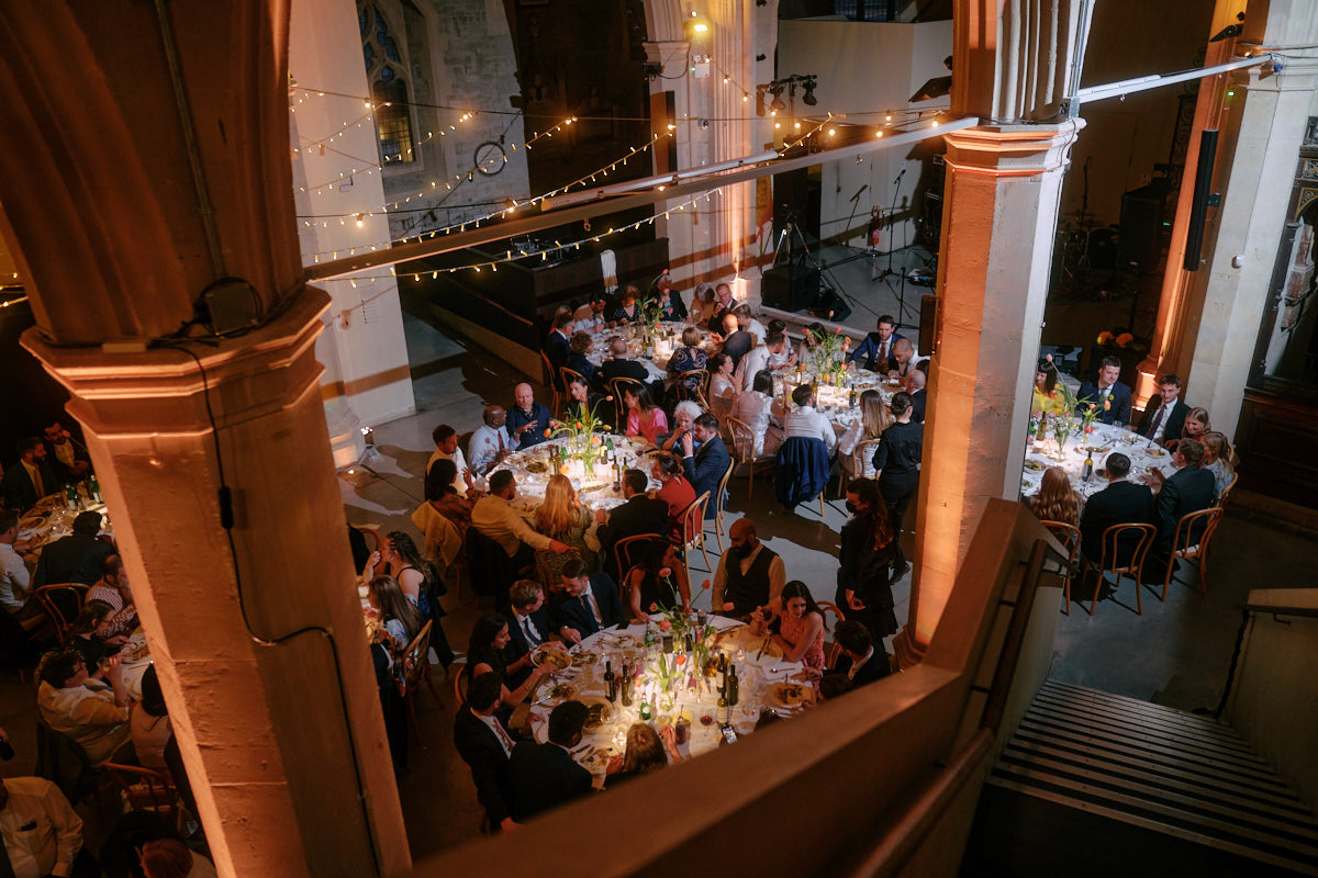 Evening wedding breakfast in the nave at Garden Museum in London. the view is taken from above and looks down at wedding guests enjoying their meal. 