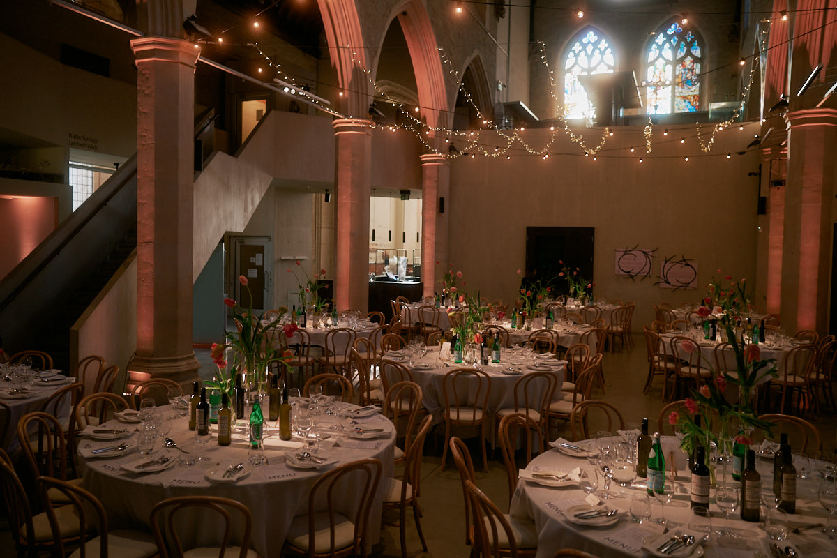 Interior of Garden Museum in London. An atmospheric photo of a dinner dinner setting of table and chairs and soft light. The decor is white and modern with traditional medieval features