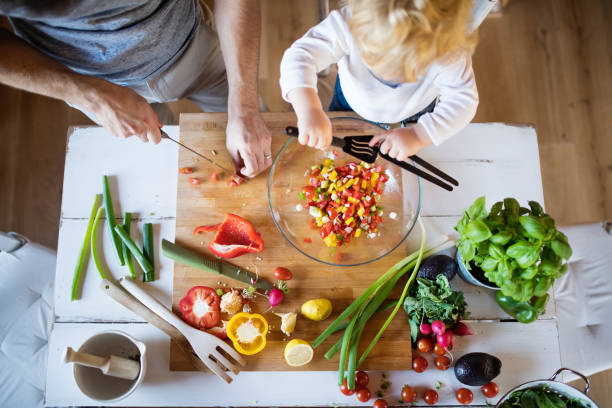An adult and a child are cutting vegetables together