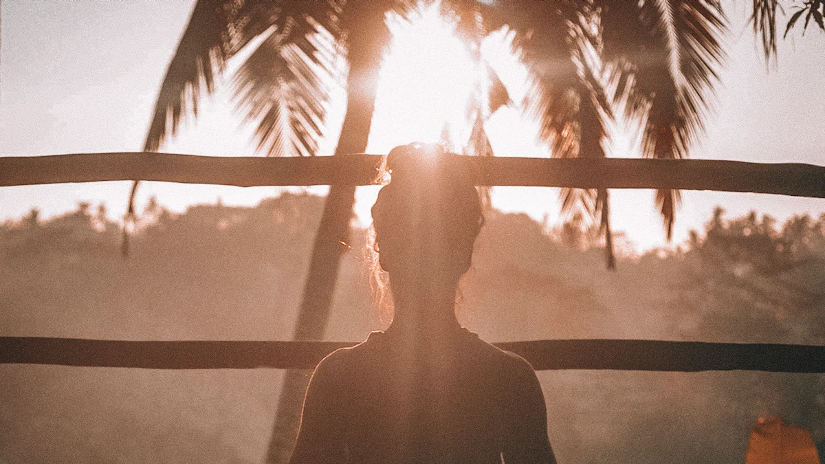 A silhouetted person stands in front of a wooden fence with palm trees and a setting sun in the background, offering a serene moment that could be straight out of a guide to mental wellness.