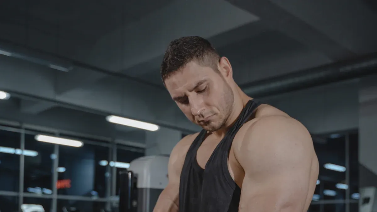 Muscular man showing strong arms while working out in gym, wearing black sleeveless sports vest, focusing on training muscles, embodying male fitness image of strength and health.